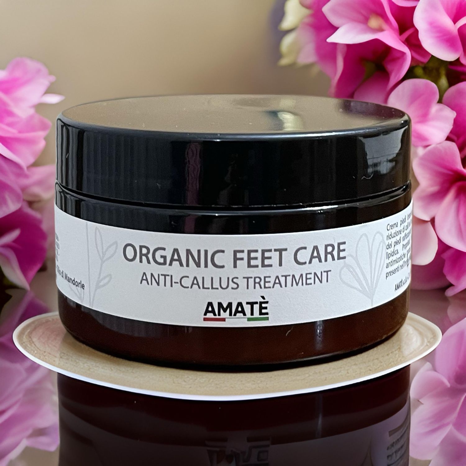Vasetto marrone scuro con coperchio nero. Scritta: ORGANIC FEET CARE ANTI-CALLUS TREATMENT. Marchio: AMATÈ. Su sottobicchiere.