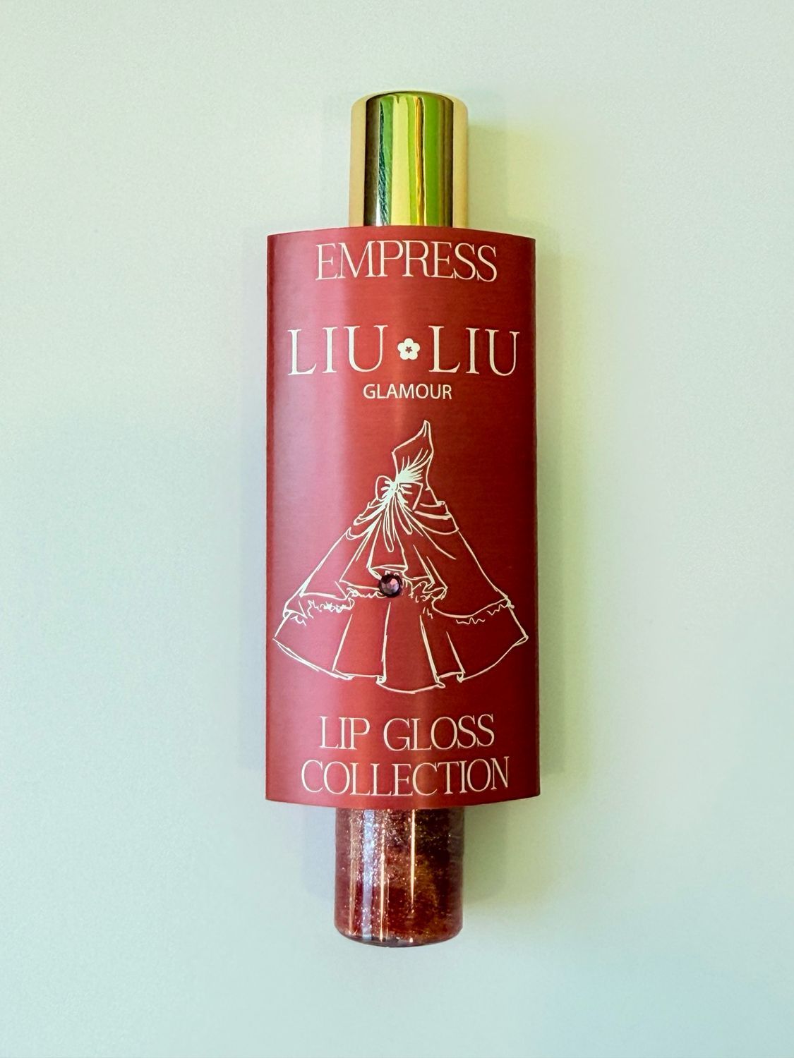 Confezione e flacone di lucidalabbra. Scritta: EMPRESS LIU LIU Glamour. Lucidalabbra rosso con tappo dorato.