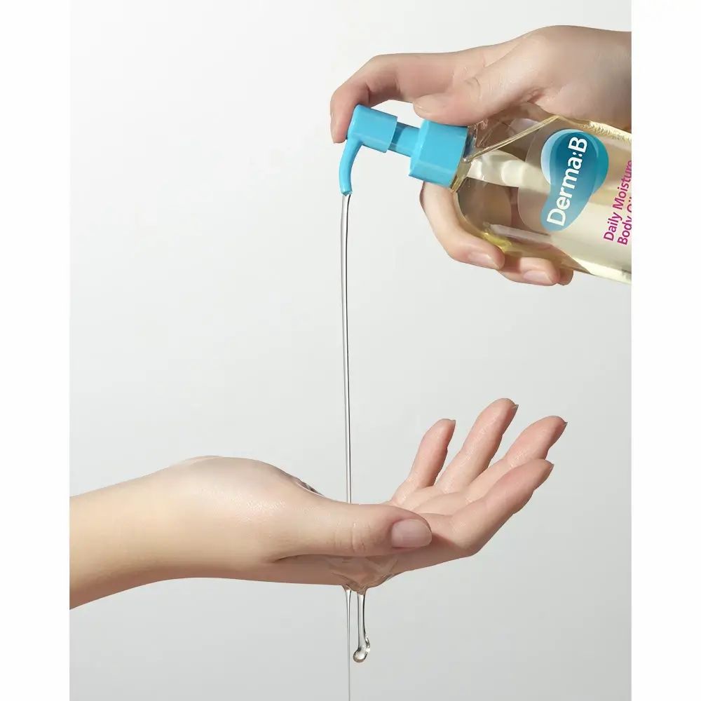 Mani che tengono un flacone di olio per il corpo. L'olio viene versato nella mano. Scritta: Derma:B Daily Moisture Body Oil.