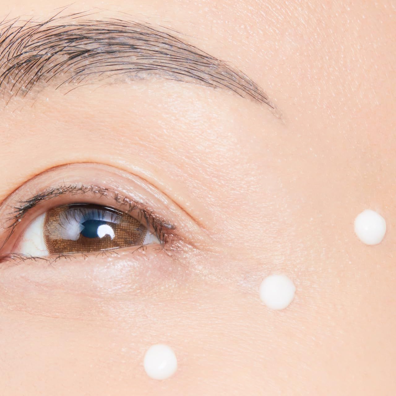 Primo piano di un occhio con tre punti di crema bianca sotto. Colore della pelle, sopracciglio e ciglia visibili.