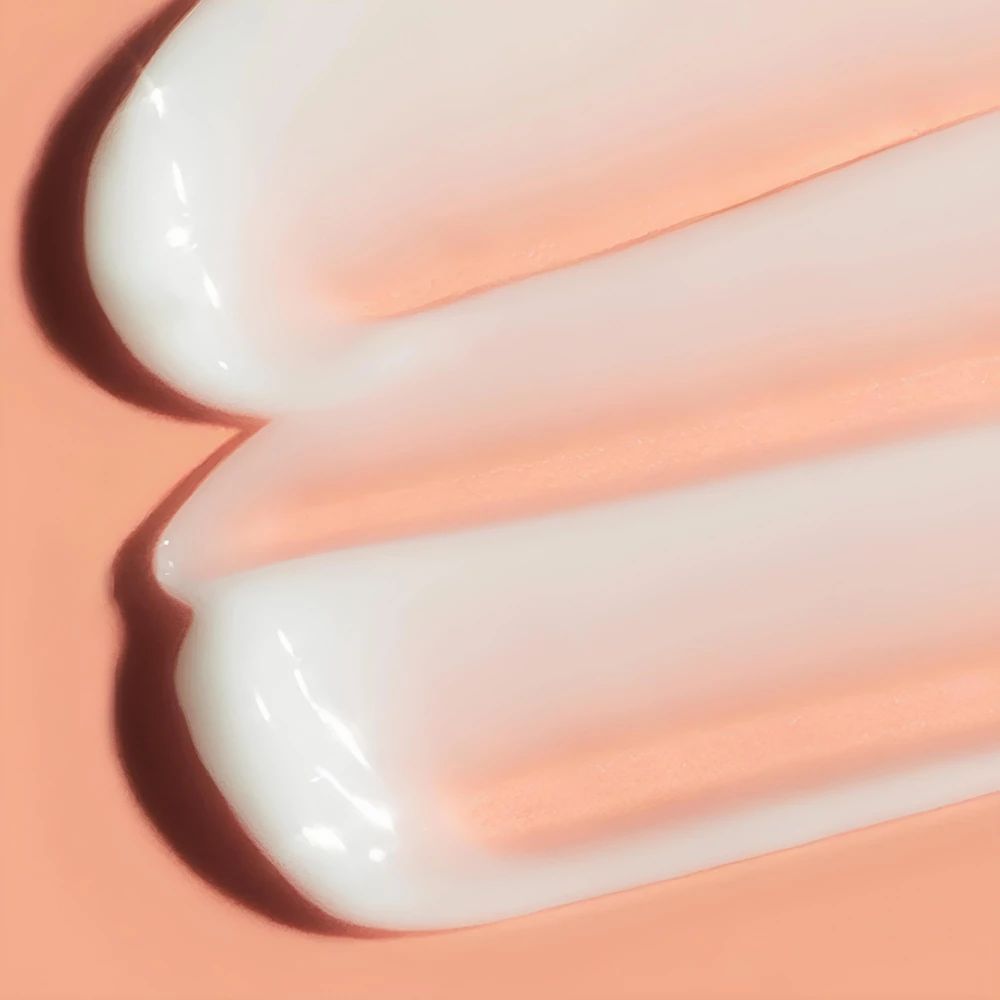 Primo piano di due strisce di crema. Crema bianca su sfondo rosa.