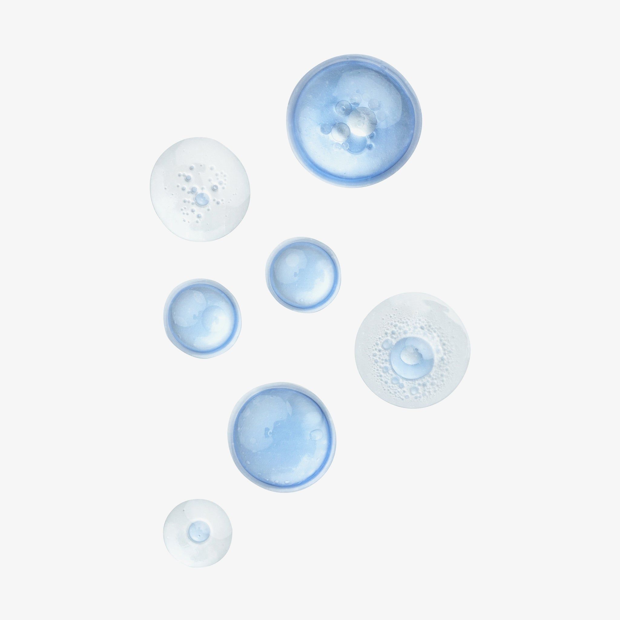 Diverse gocce blu e trasparenti su sfondo bianco. Dimensioni e forme diverse. Alcune gocce sono schiumose.