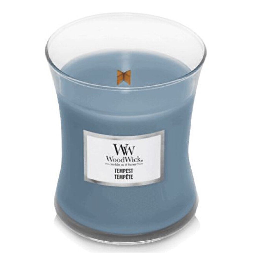 Candela a clessidra con coperchio in vetro. Cera blu, etichetta rettangolare con logo e testo. Stoppino in legno visibile.