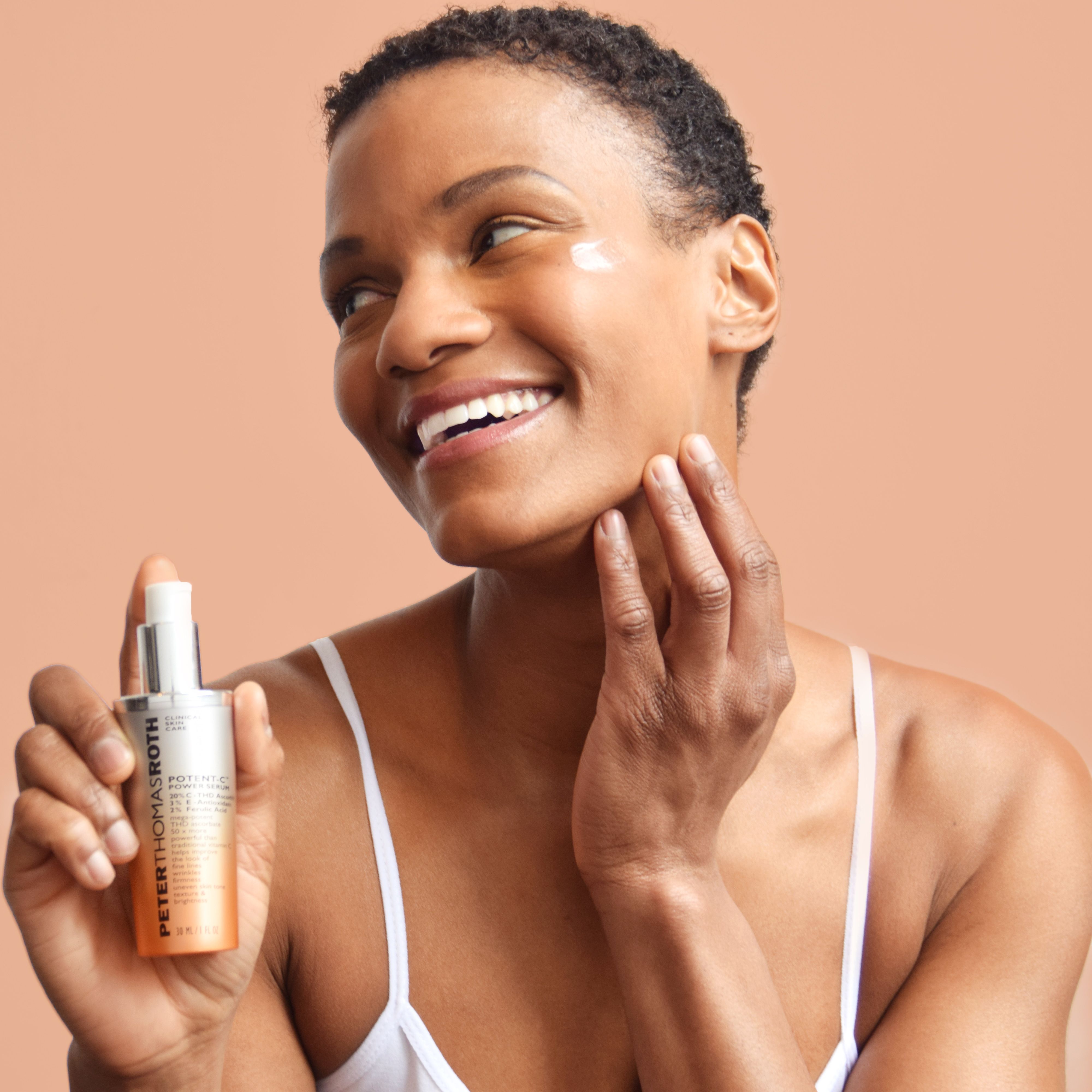 Donna che tiene in mano un flacone di siero. Scritta: Potent-C Power Serum. Tappo argentato e sfumatura arancione. La donna si tocca il viso.