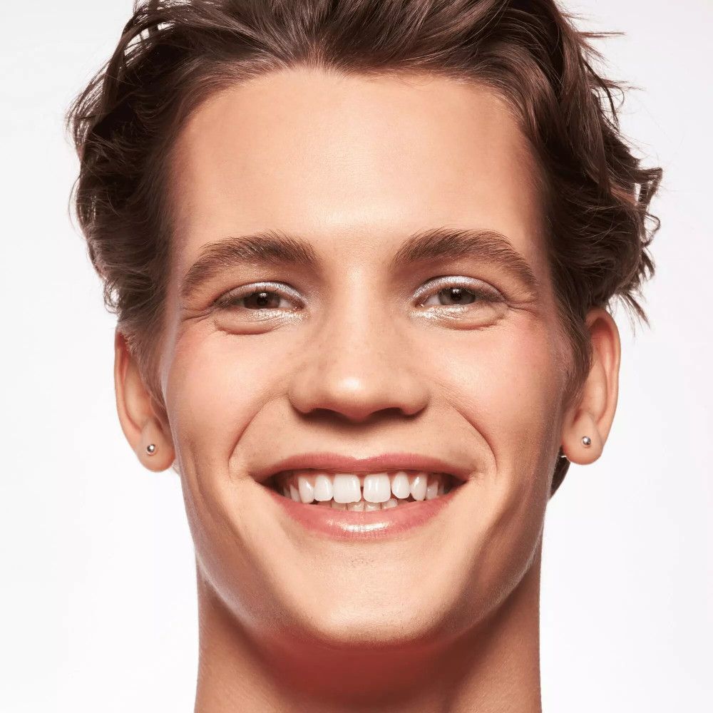 Ritratto di un uomo con la pelle chiara. Sorride. Indossa orecchini.