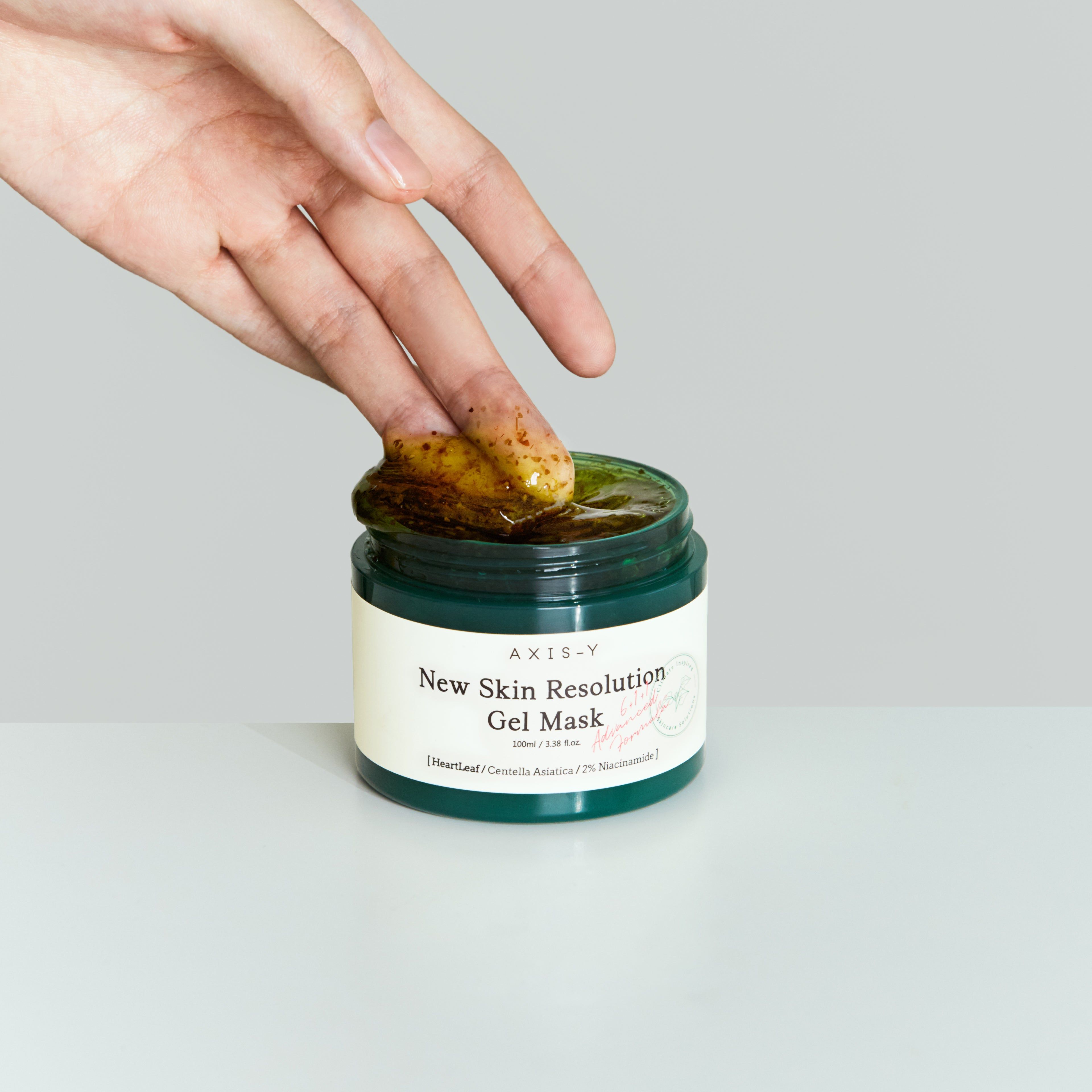 Mano che immerge un dito in un barattolo verde di maschera. Scritta: New Skin Resolution Gel Mask.