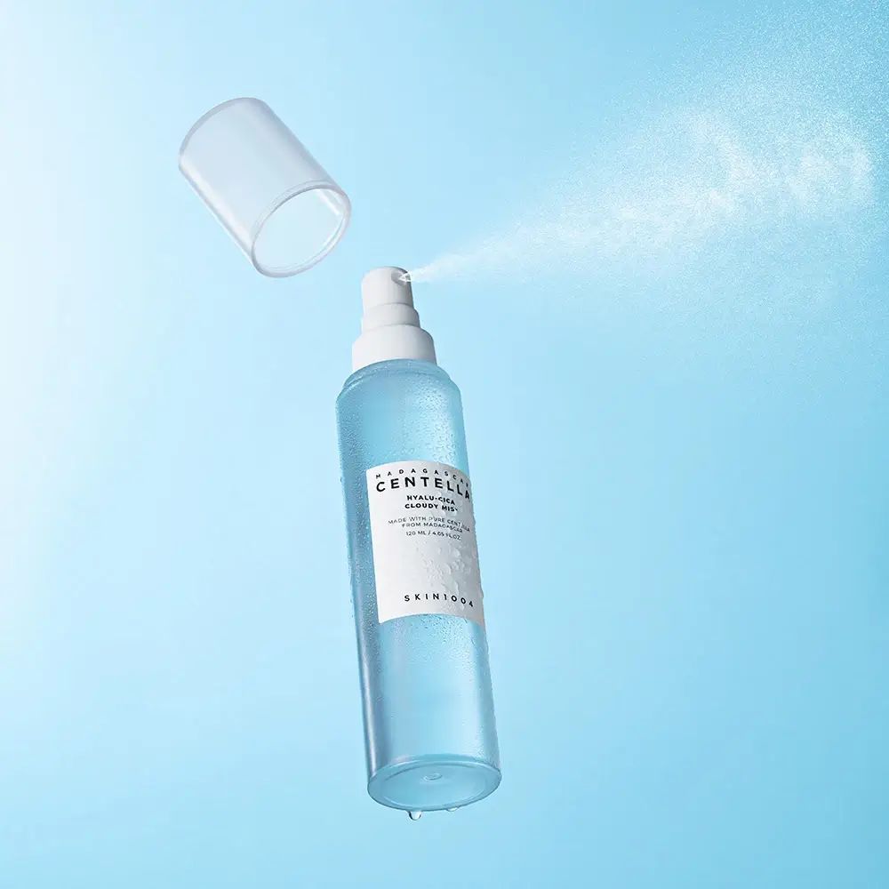 Flacone spray blu trasparente, spruzzo. Scritta: MADAGASCAR CENTELLA, HYALU-CICA Cloudy Mist. SKIN1004. Coperchio accanto.