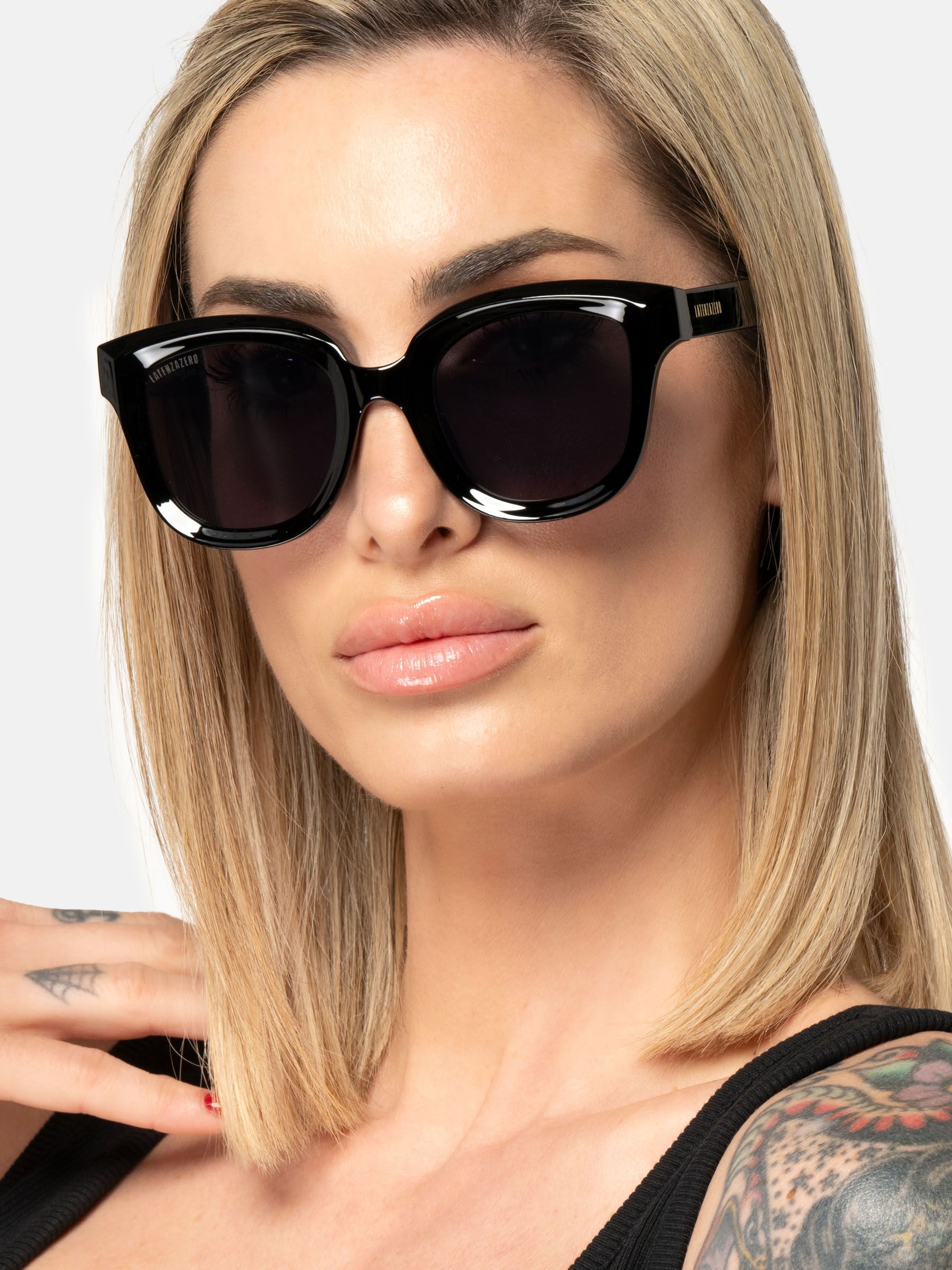 Donna con occhiali da sole neri. Lenti scure, forma rettangolare. Logo Latenzazero sull'asta.