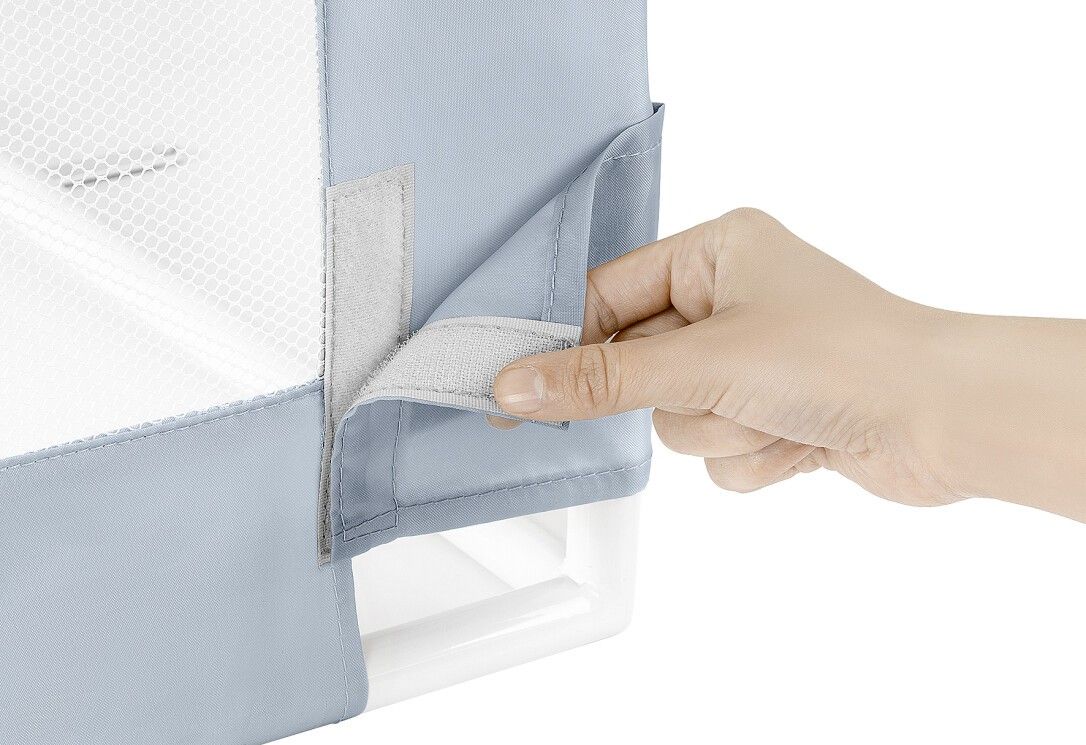 Mano che apre il velcro sulla barriera letto blu. Rete bianca visibile.