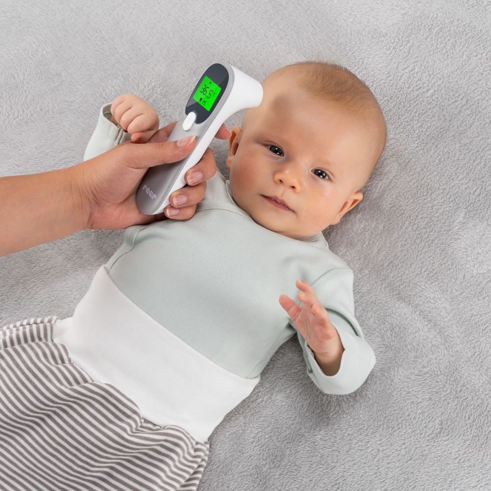 Persona misura la temperatura di un bambino con un termometro a infrarossi. Il termometro mostra 36,5°C. Marchio: reer.