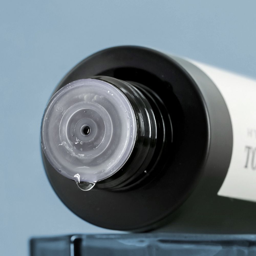 Primo piano del collo di un toner con tappo nero e chiusura trasparente. Una goccia di liquido pende.