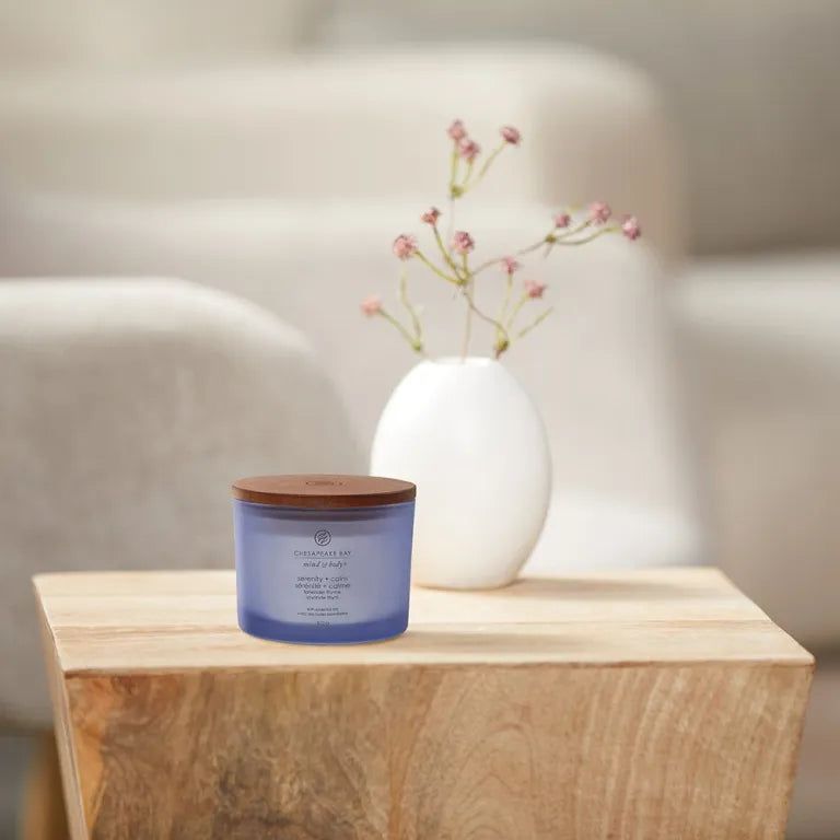 Candela blu con coperchio in legno. Scritta 'Chesapeake Bay'. Su tavolo legno, vicino vaso con fiori.