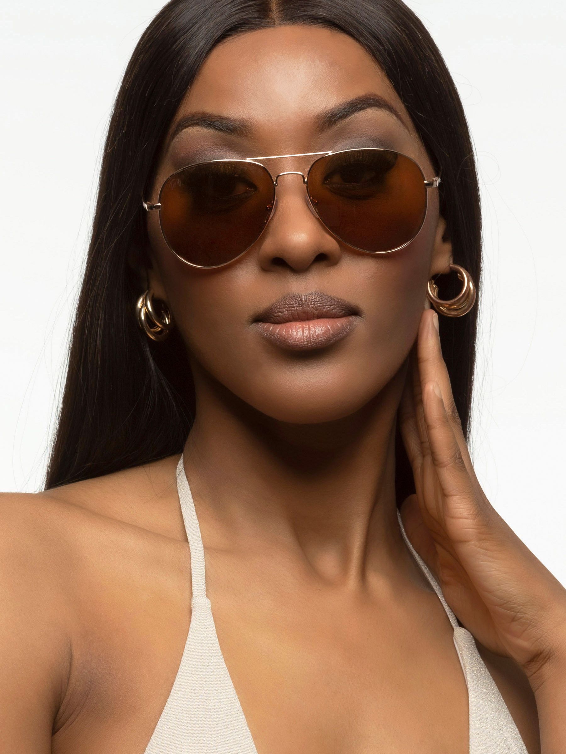 Donna con occhiali da sole Twig. Montatura dorata, lenti marroni. Primo piano.