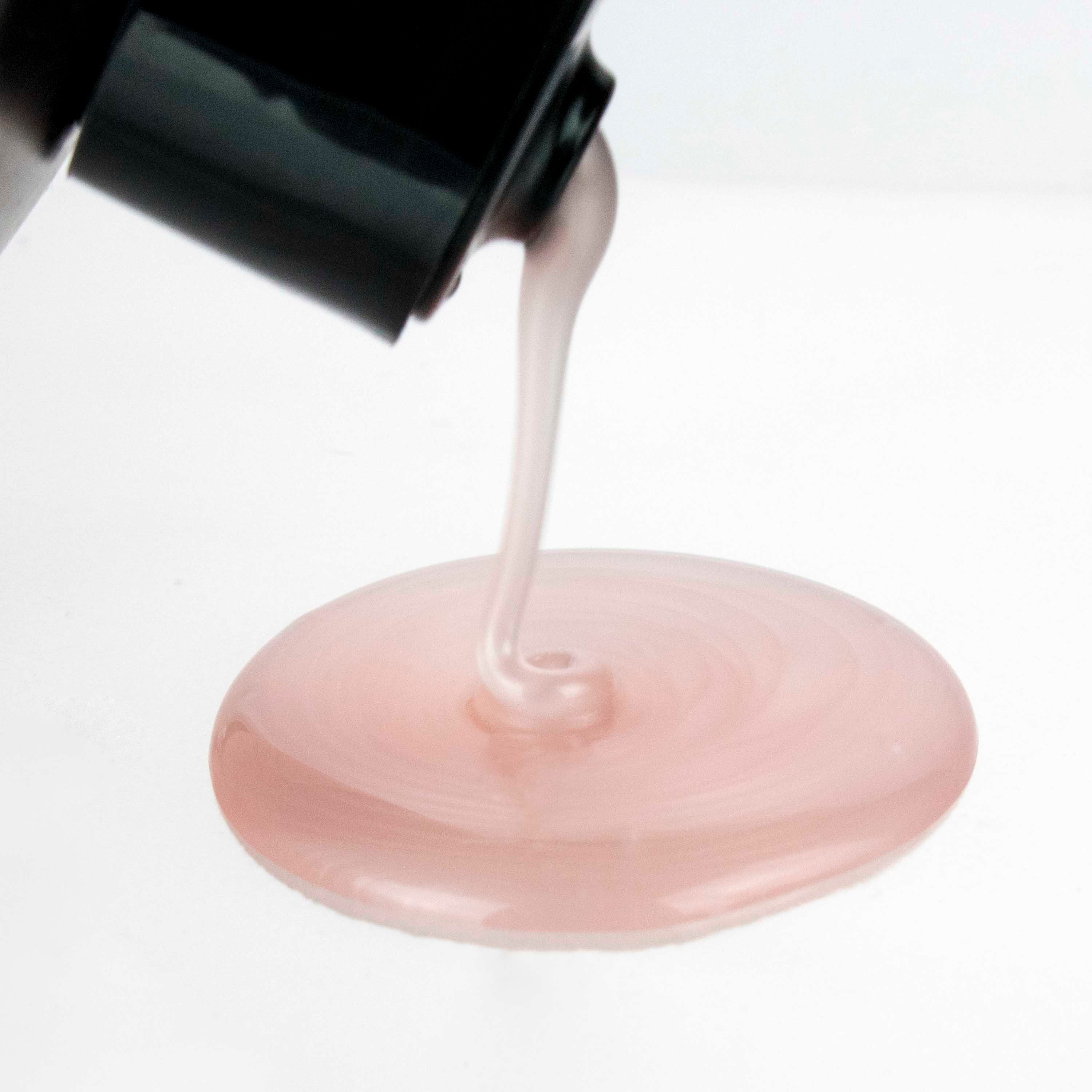 Shampoo rosa che fuoriesce da un flacone nero. Lo sfondo è bianco. Il liquido forma un piccolo lago.
