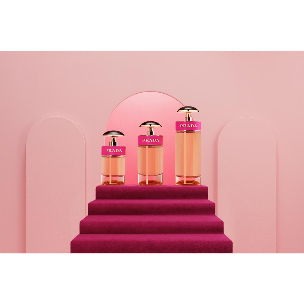 Tre flaconi di profumo su una scala. Sfondo rosa. Flaconi con elementi dorati e fascia rosa.