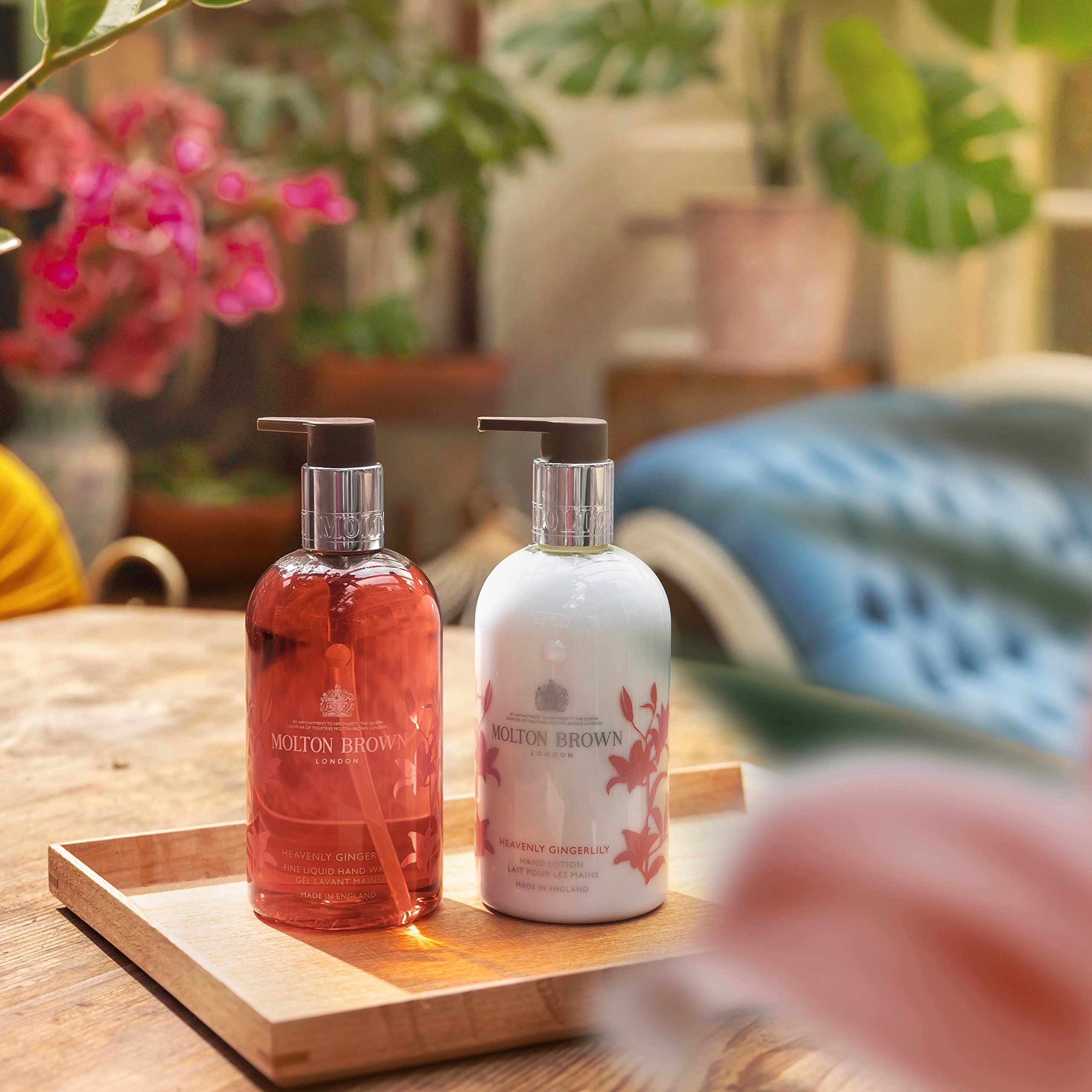 Vassoio in legno con due saponi liquidi. Flaconi rosso e bianco con dosatore. Scritta: Molton Brown. Piante sullo sfondo.