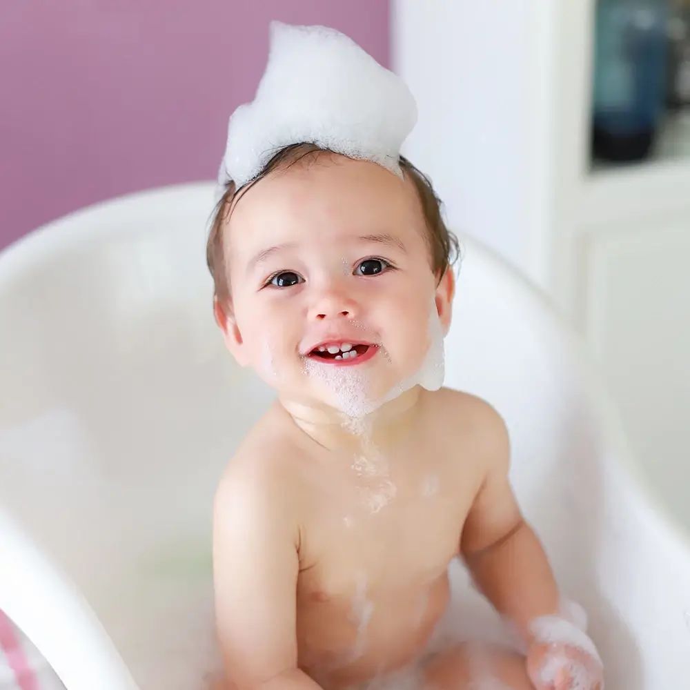 Bambino in vasca da bagno con schiuma sulla testa. Il bambino sorride.