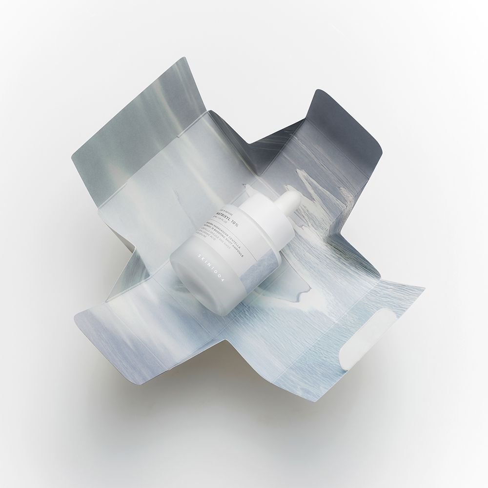 Confezione del prodotto. Scatola aperta con flacone. Motivo blu e bianco. Flacone con pipetta.