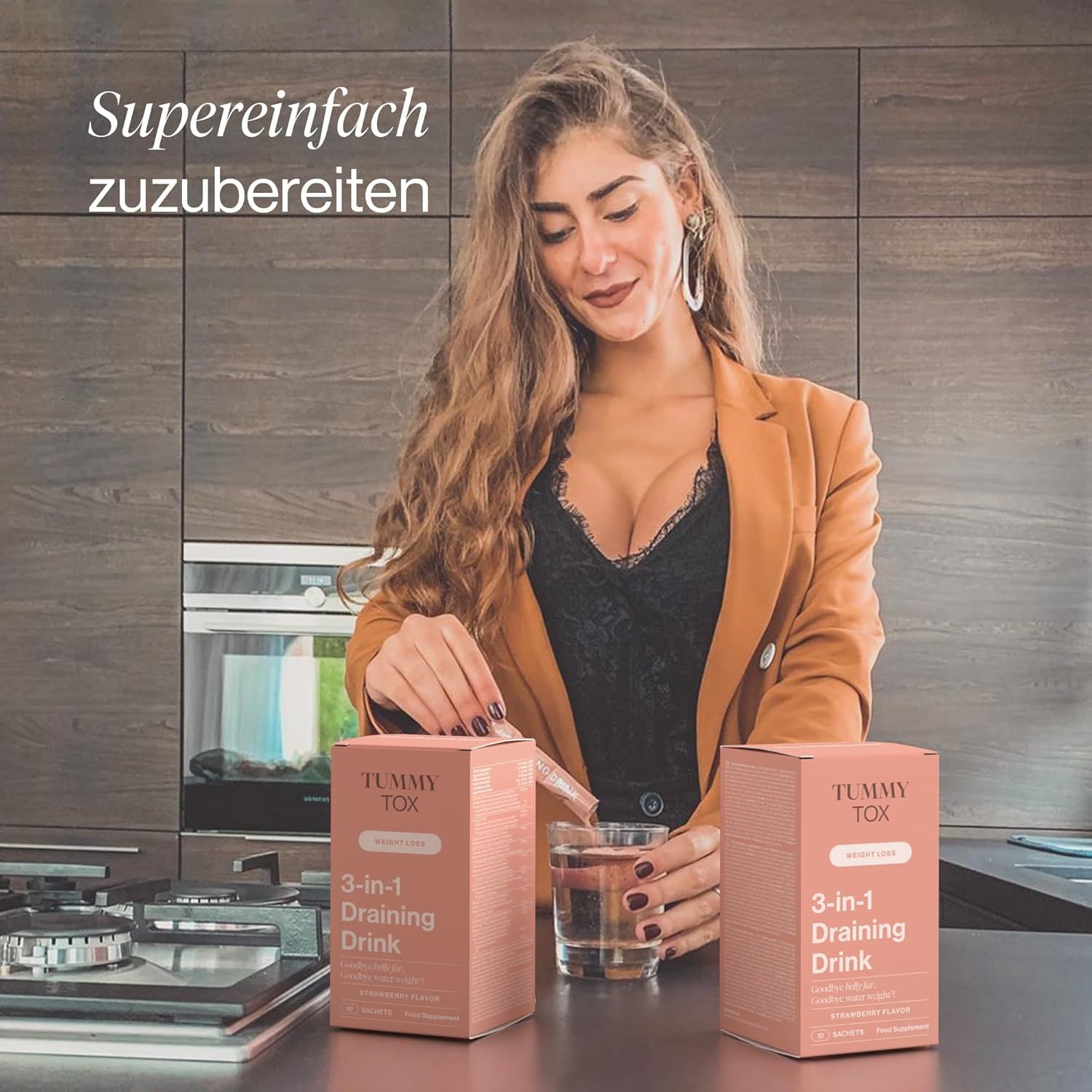 Donna in cucina con due confezioni di Tummy Tox 3-in-1 Draining Drink e un bicchiere d'acqua.