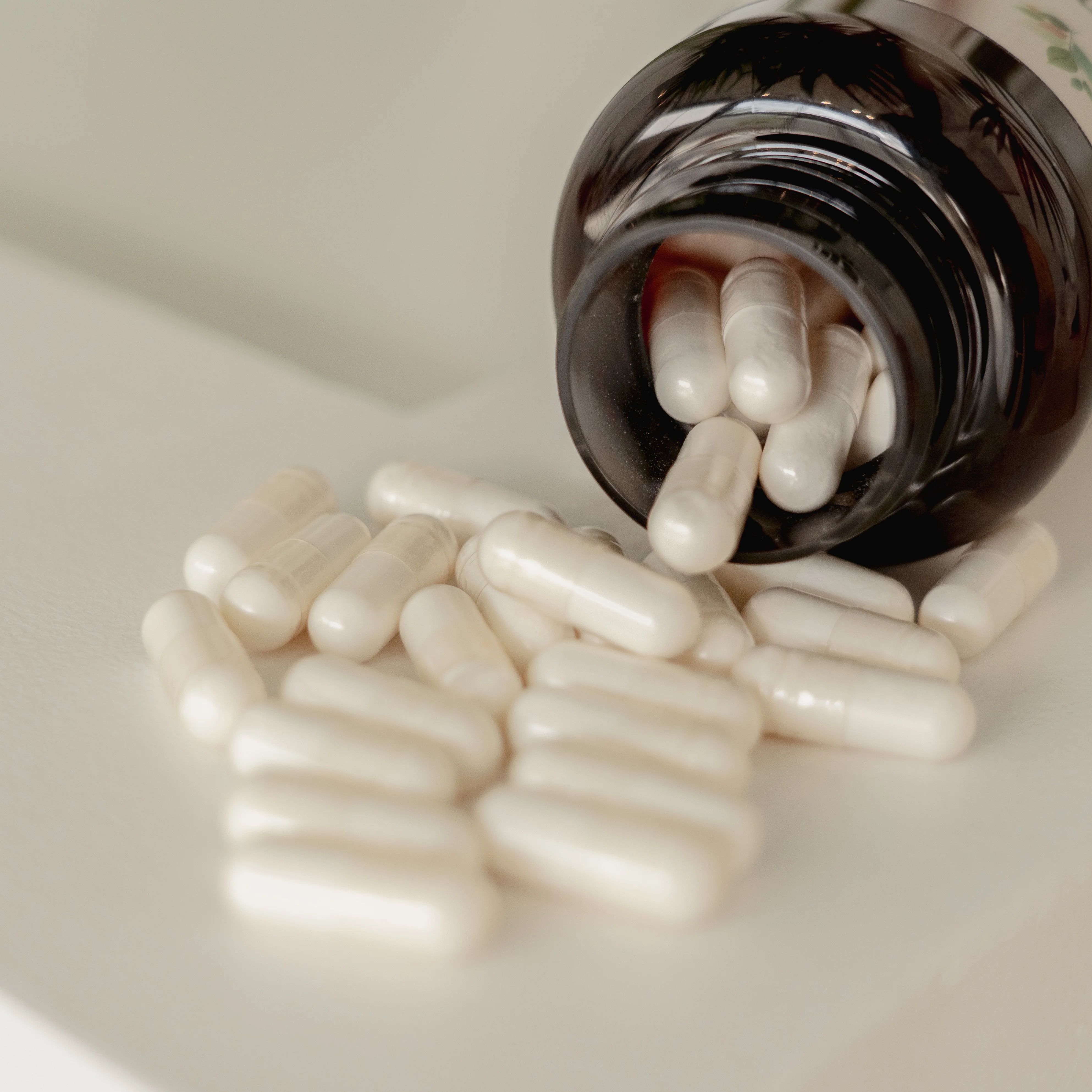 Capsule bianche accanto a un flacone marrone aperto. Capsule visibili.