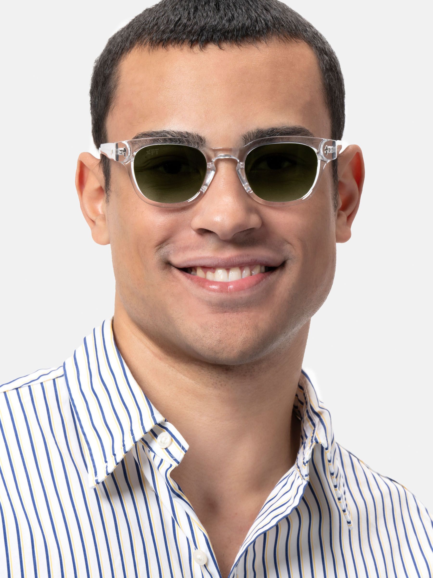 Uomo con occhiali da sole trasparenti e lenti verdi. Sorridente, indossa una camicia a righe.