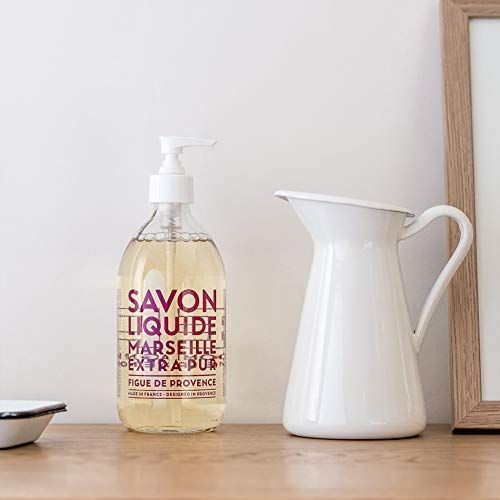 Sapone liquido Marsiglia accanto a una brocca bianca e una cornice. Il sapone è su una superficie di legno.