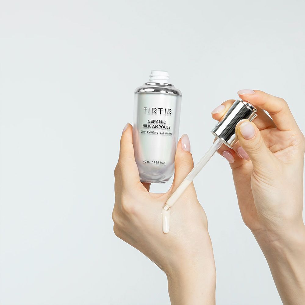 Mani che applicano TIRTIR Ceramic Milk Ampoule, con gocce sulla pelle.