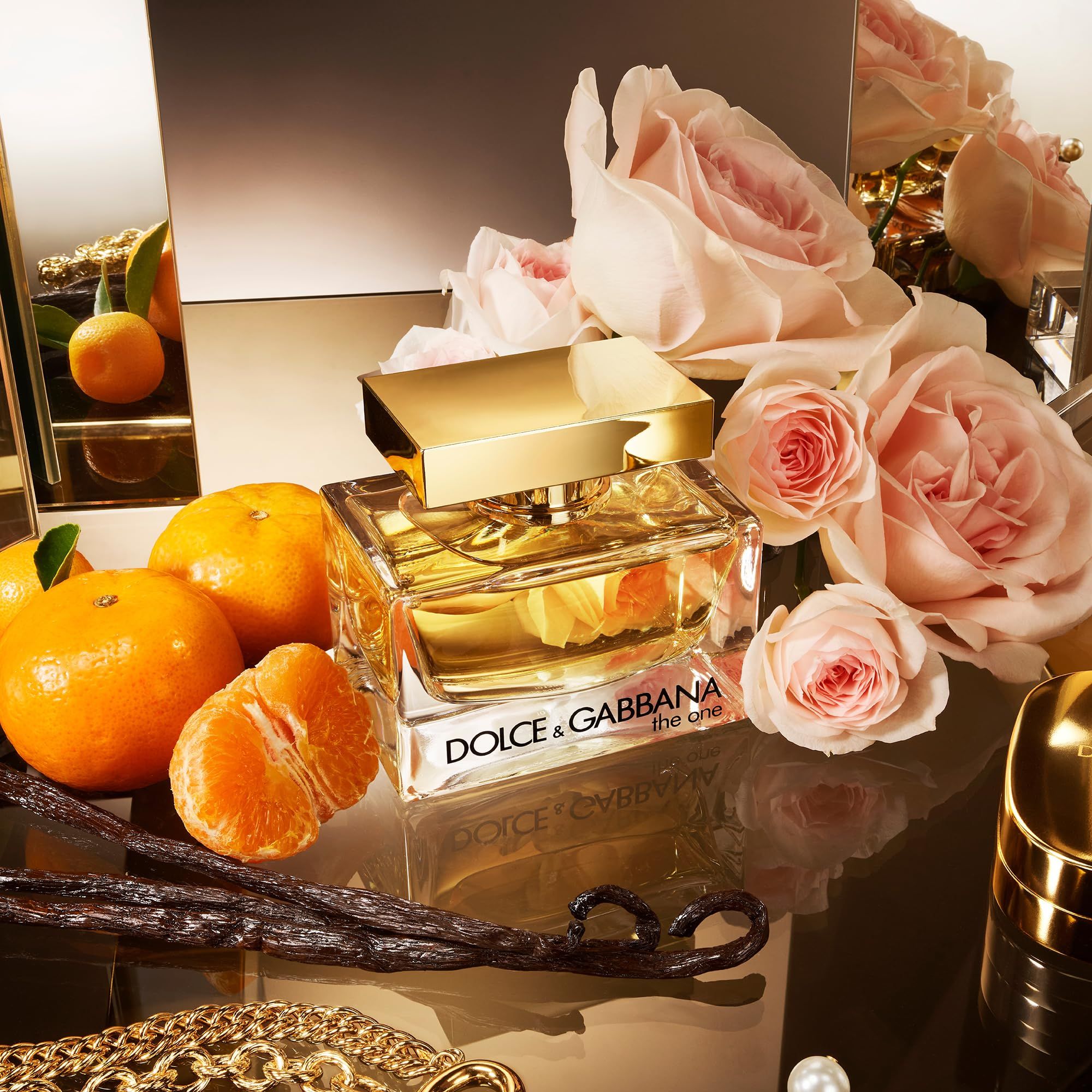 Flacone in vetro con tappo dorato, circondato da rose, mandarini e baccelli di vaniglia. Scritta: Dolce & Gabbana, the one.