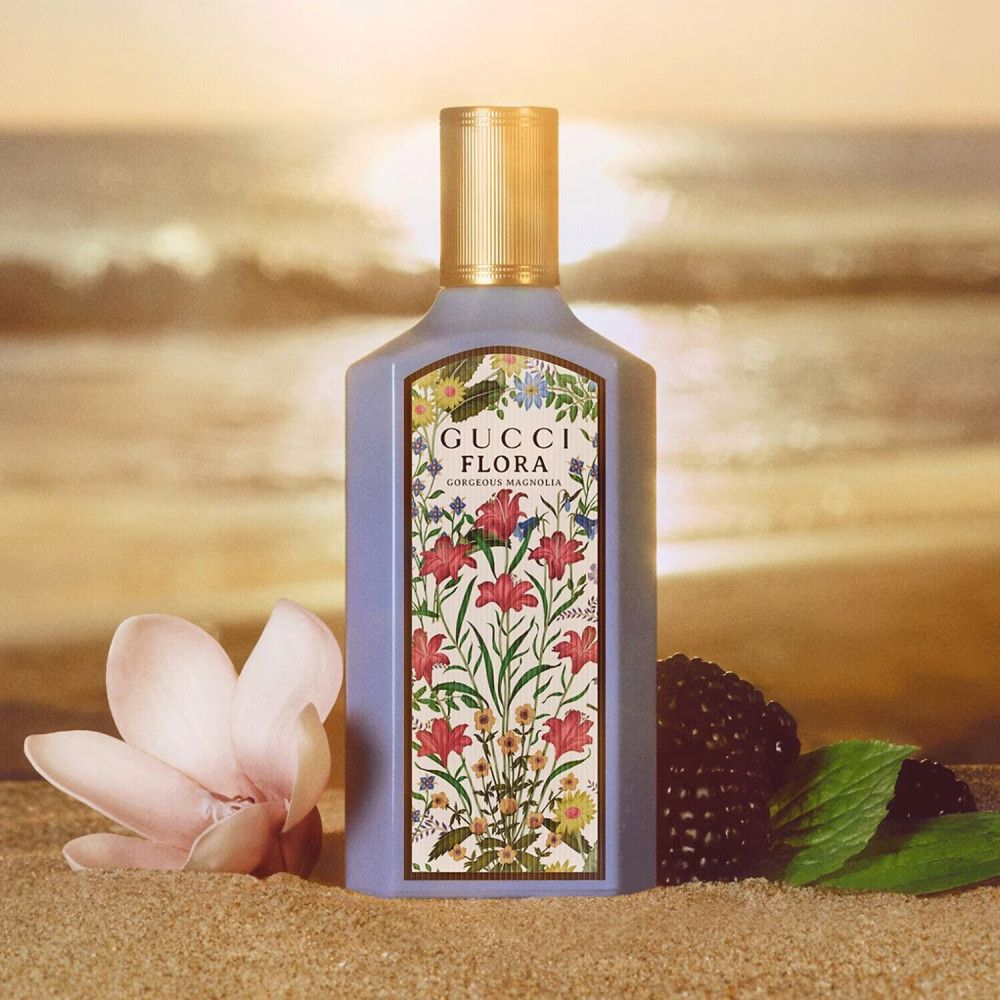 Flacone Gucci Flora Gorgeous Magnolia con etichetta floreale. Tappo dorato. Sfondo spiaggia.