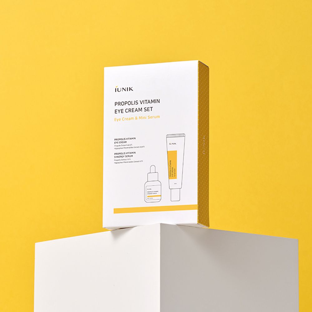 iUNIK Propolis Vitamin Eye Cream Set. Confezione su piedistallo bianco, sfondo giallo. Testo sulla confezione.
