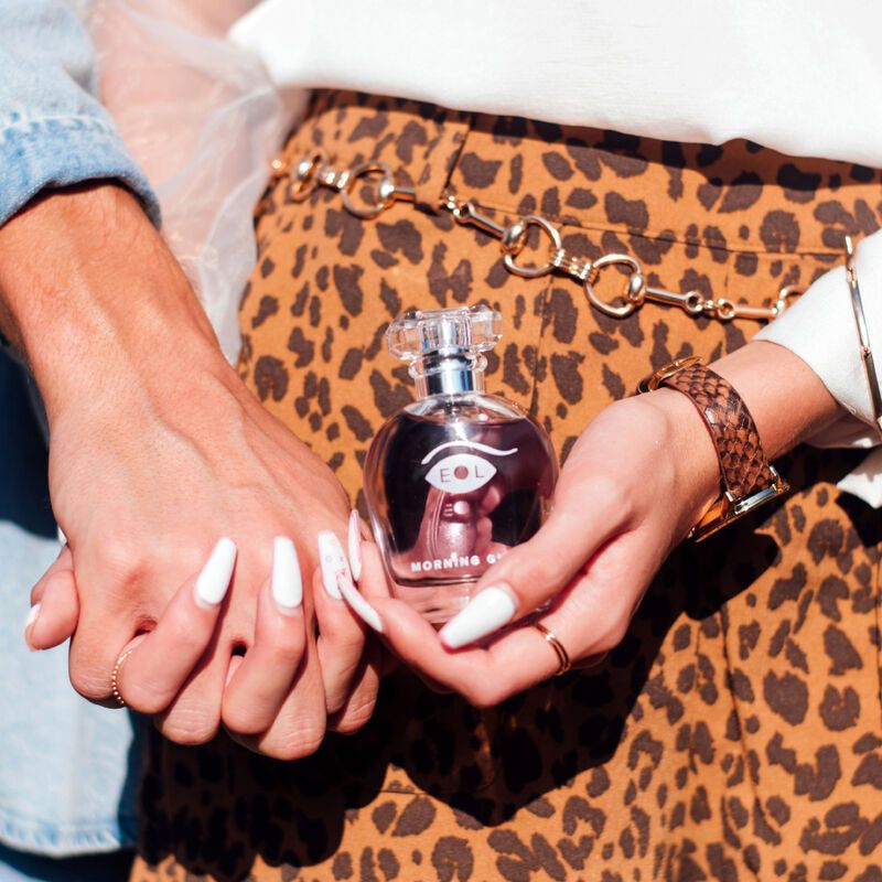 Due mani che tengono un flacone. Il flacone ha liquido rosa, collo argentato e tappo trasparente. Scritte "EOL" e "MORNING GLOW".