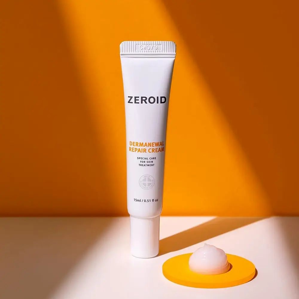 Tubo di crema bianco con scritta: ZEROID, Dermanewal Repair Cream. 15ml/0.51 fl oz. Su supporto giallo.