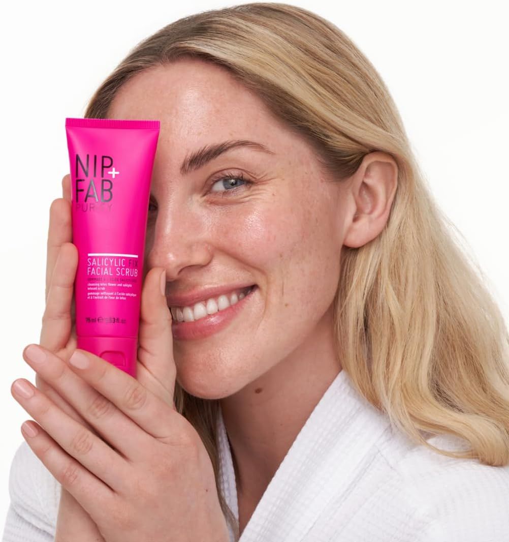 Donna tiene un tubo rosa davanti al viso. Il tubo reca la scritta "NIP+FAB" e "Salicylic Facial Scrub".
