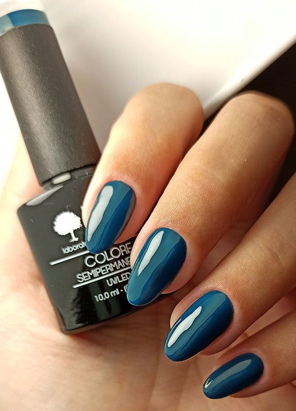 Mano con unghie smaltate di verde scuro. Accanto, flacone di smalto. Scritta: Colore Semipermanente.