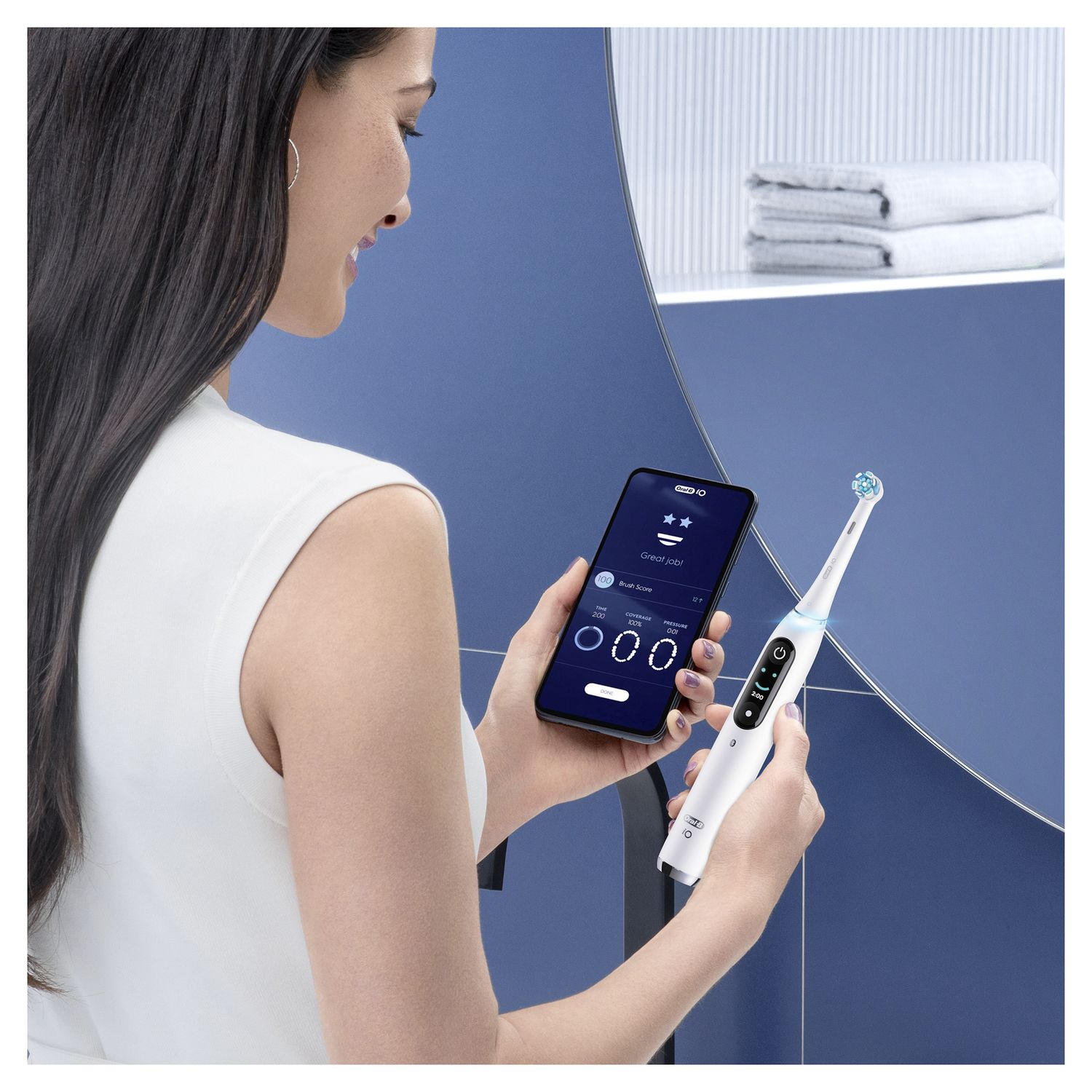 Donna tiene in mano uno smartphone e uno spazzolino elettrico iO 9 bianco. Lo schermo dello smartphone mostra dati.