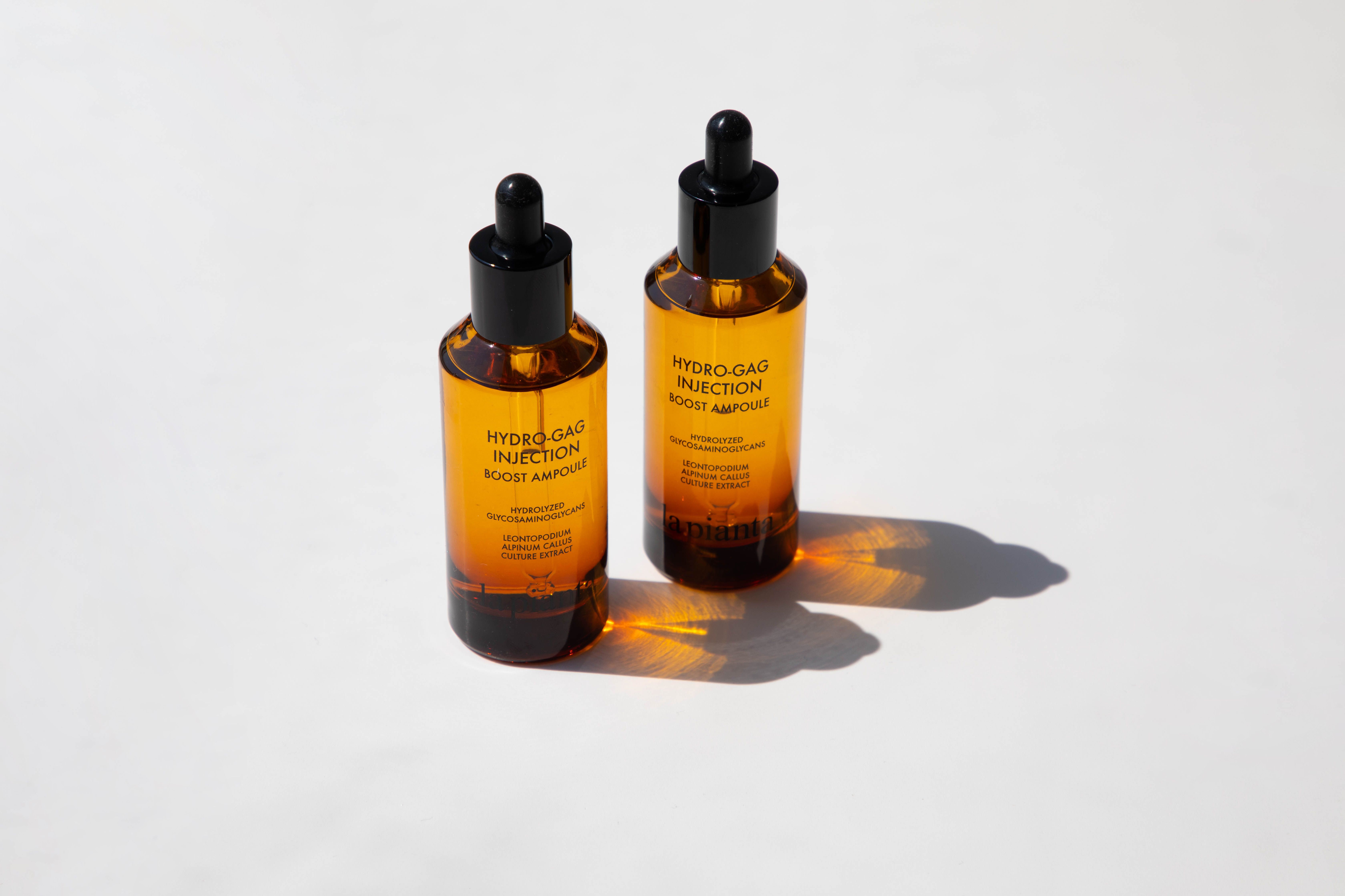 Due flaconi di vetro marrone con contagocce nero. Scritta: HYDRO-GAG INJECTION BOOST AMPOULE. Marchio: la pianta.