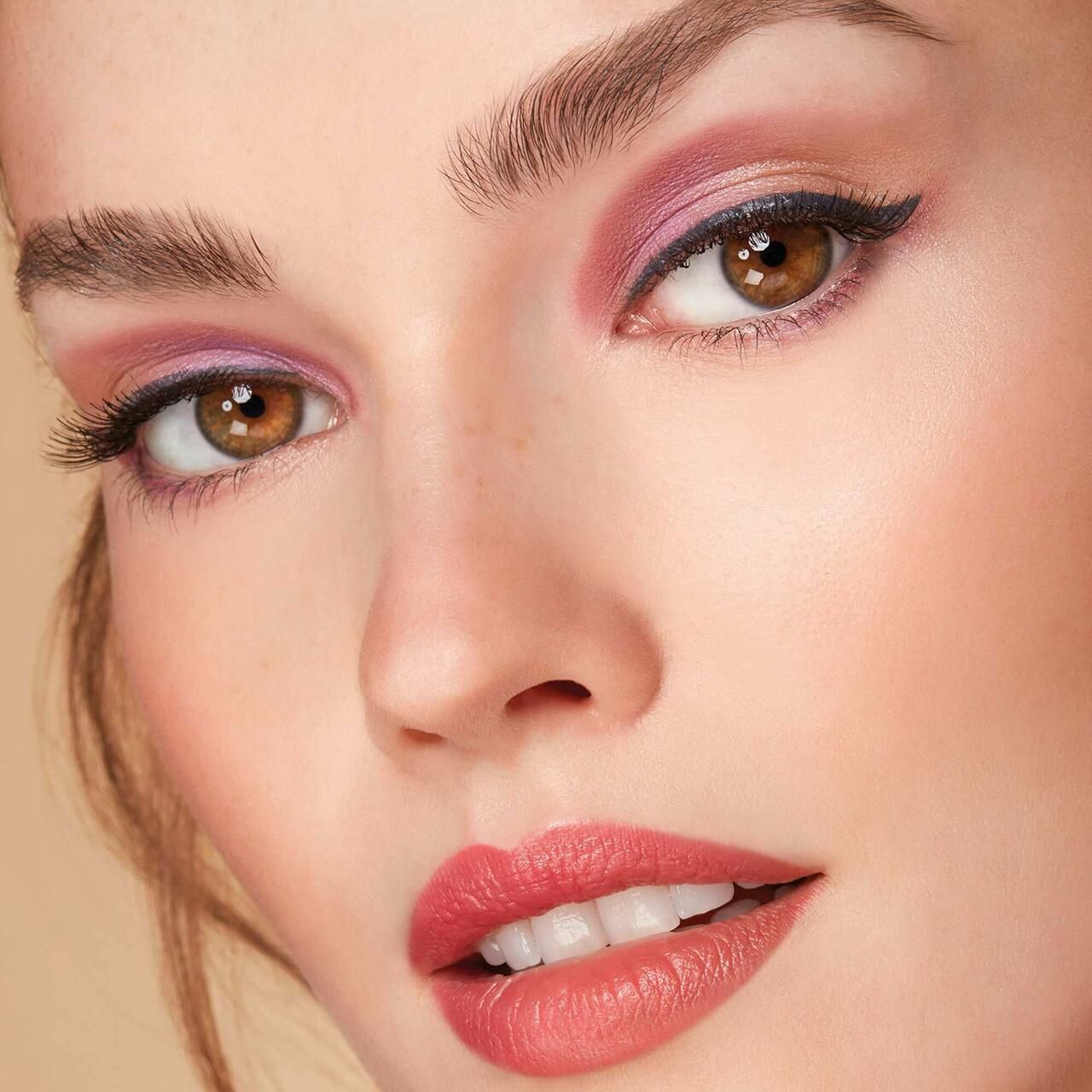 Primo piano di un viso con ombretto rosa. Gli occhi sono sottolineati dall'eyeliner, le labbra rosse.
