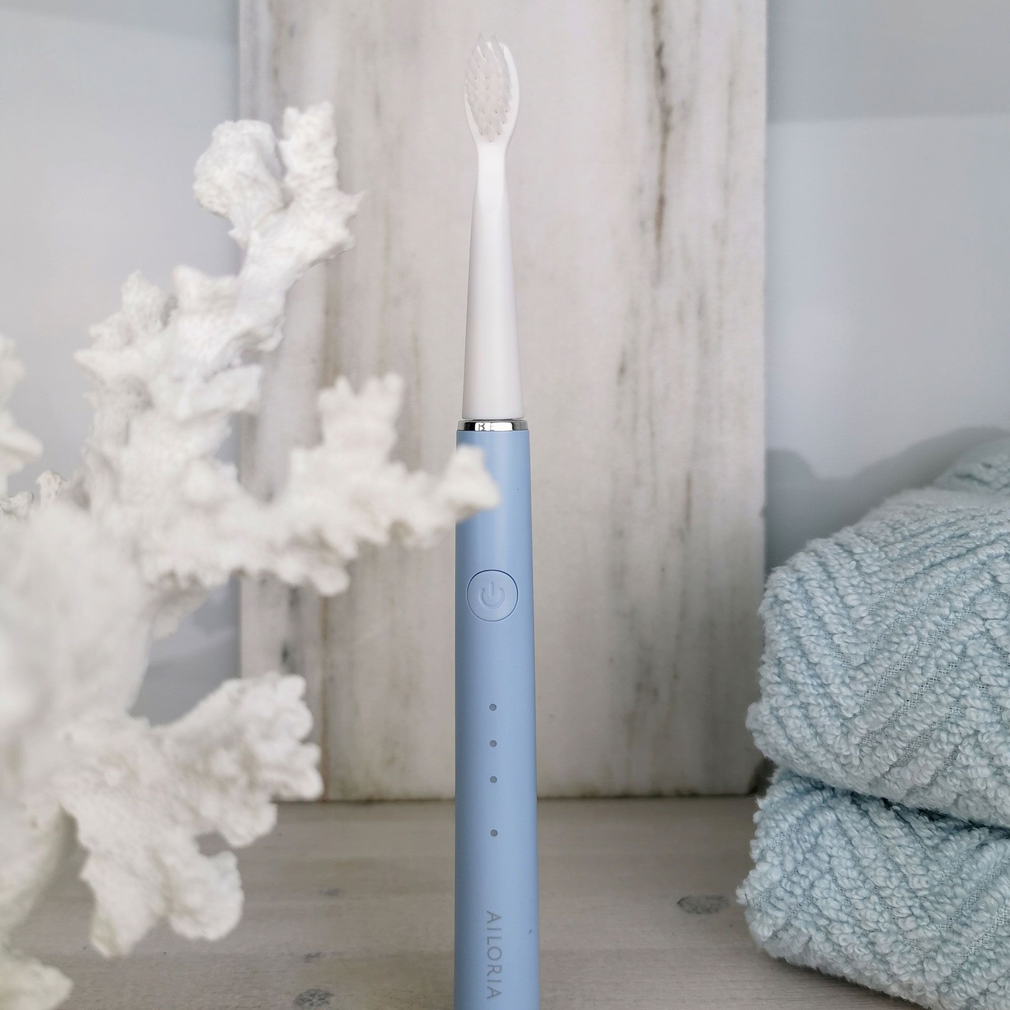 Spazzolino azzurro su sfondo bianco con decorazioni e asciugamani.