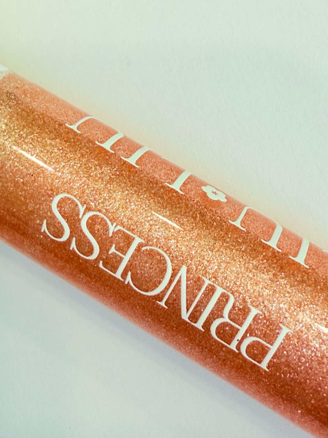 Primo piano di un lucidalabbra rosa glitterato. Scritta: PRINCESS LIU LIU. Sfondo bianco. Tappo dorato.