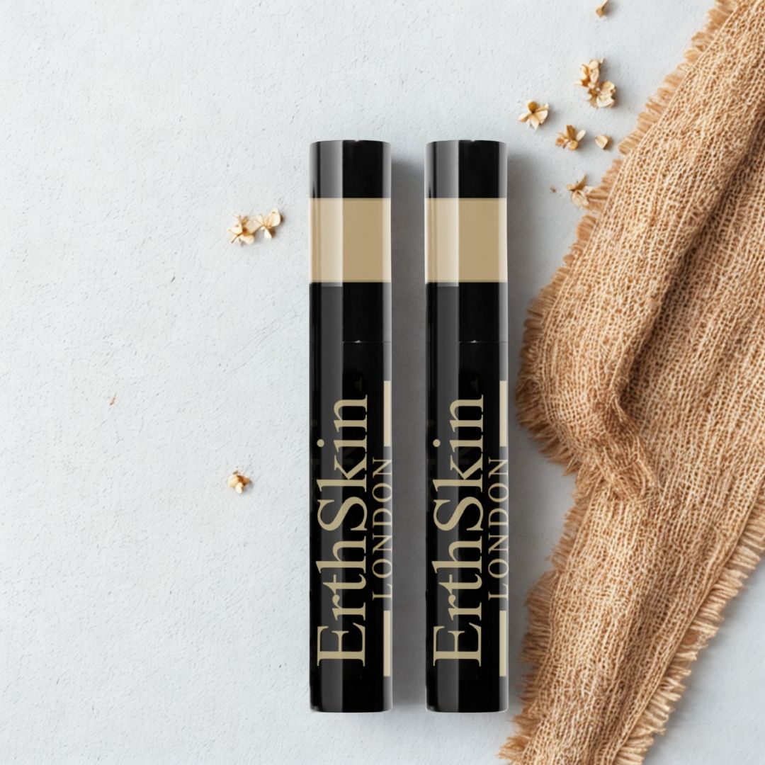 Due tubetti di mascara neri con testo dorato. Scritto: ErthSkin London. Zona beige in alto. Su sfondo chiaro con tessuto e fiori.