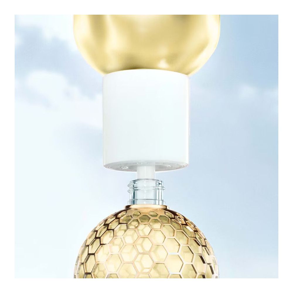 Flacone con tappo dorato e chiusura bianca. Flacone in vetro con liquido giallo. Sfondo blu.