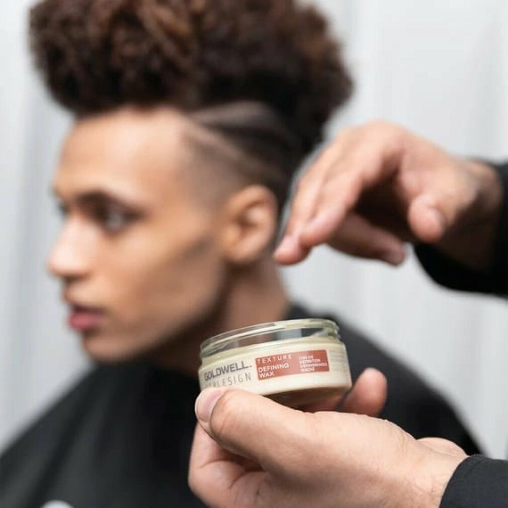Persona che tiene un vasetto di Goldwell Stylesign Texture Defining Wax. Persona con acconciatura afro sullo sfondo.