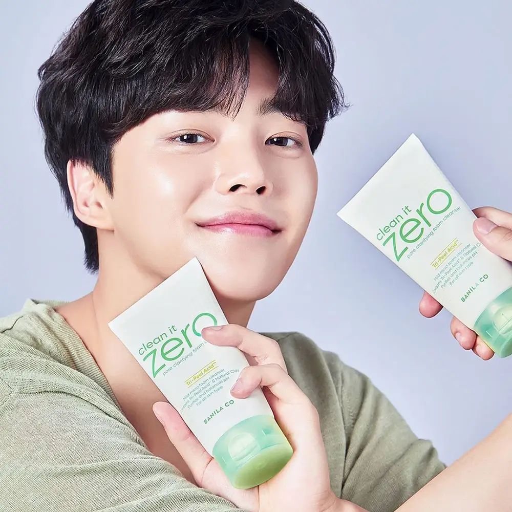 Uomo tiene due tubi. I tubi mostrano "clean it zero" e "BANILA CO". I tubi sono bianchi con accenti verdi.