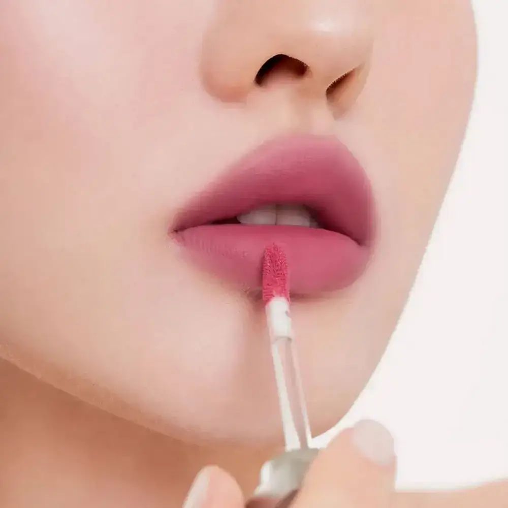 Labbra con rossetto rosa. Applicatore in mano. Primo piano.