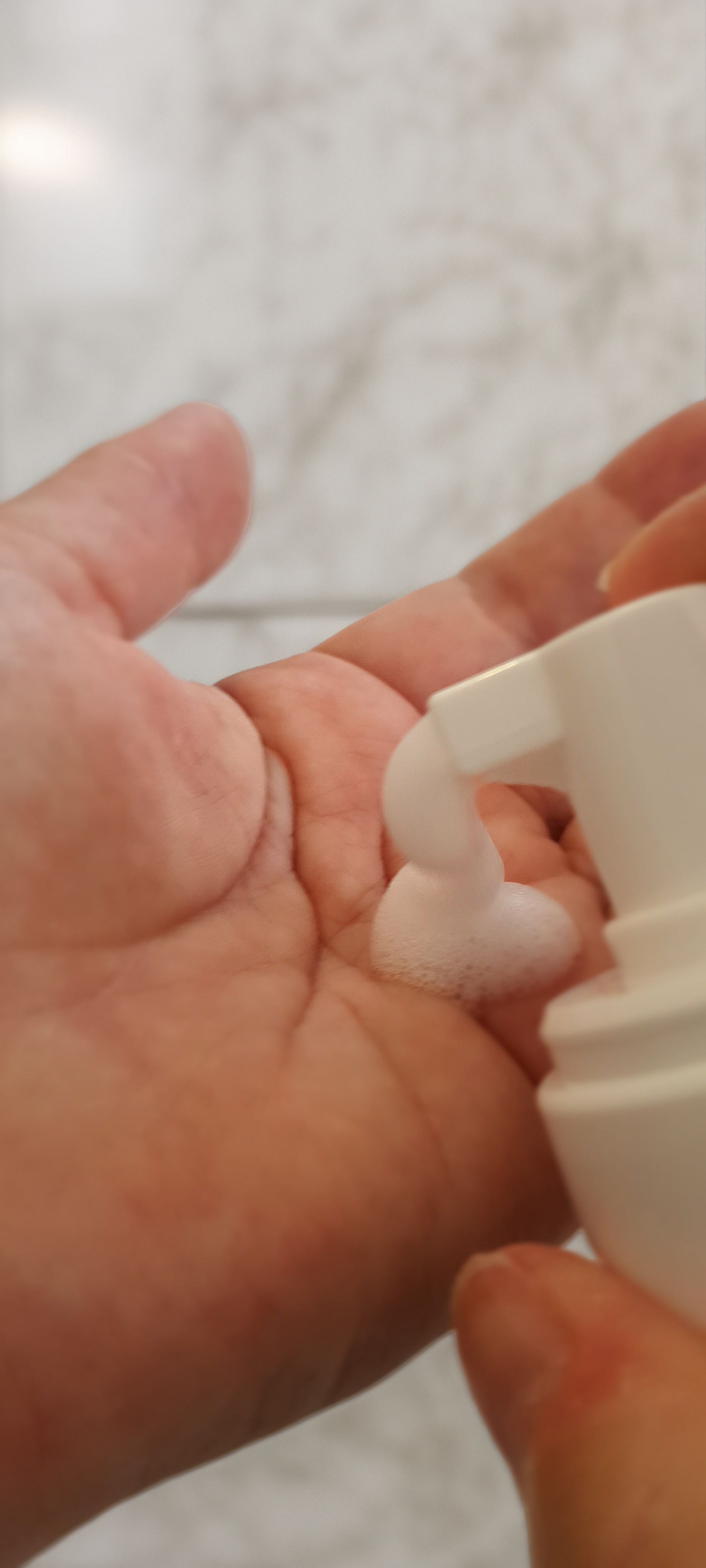 Mano che riceve schiuma da un dispenser. La schiuma è bianca e cremosa.