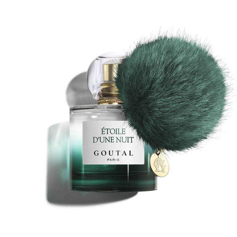 Flacone di profumo sfumato verde, tappo dorato e ciondolo. Un pompon verde è attaccato al flacone.