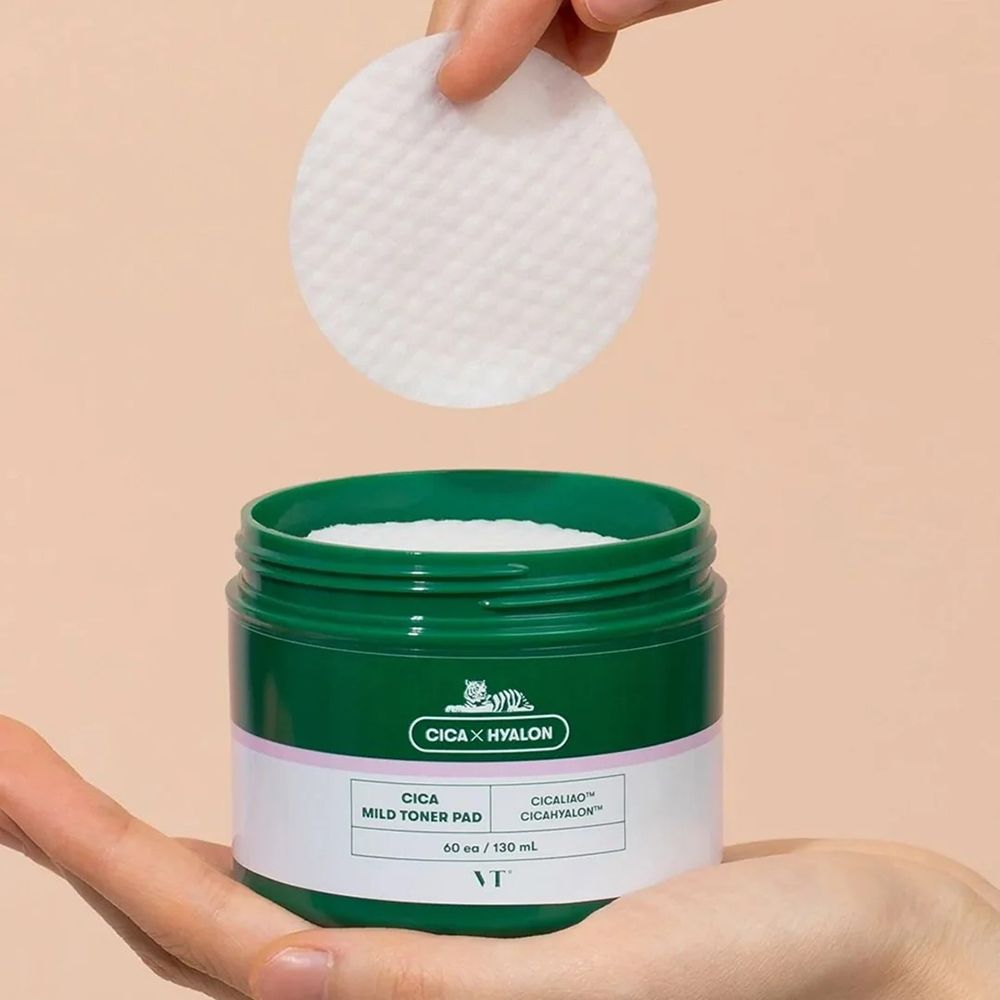 Mano che tiene un tampone tonico bianco sopra un barattolo verde aperto. Scritta: CICA x HYALON, CICA Mild Toner Pad. Marchio: VT.