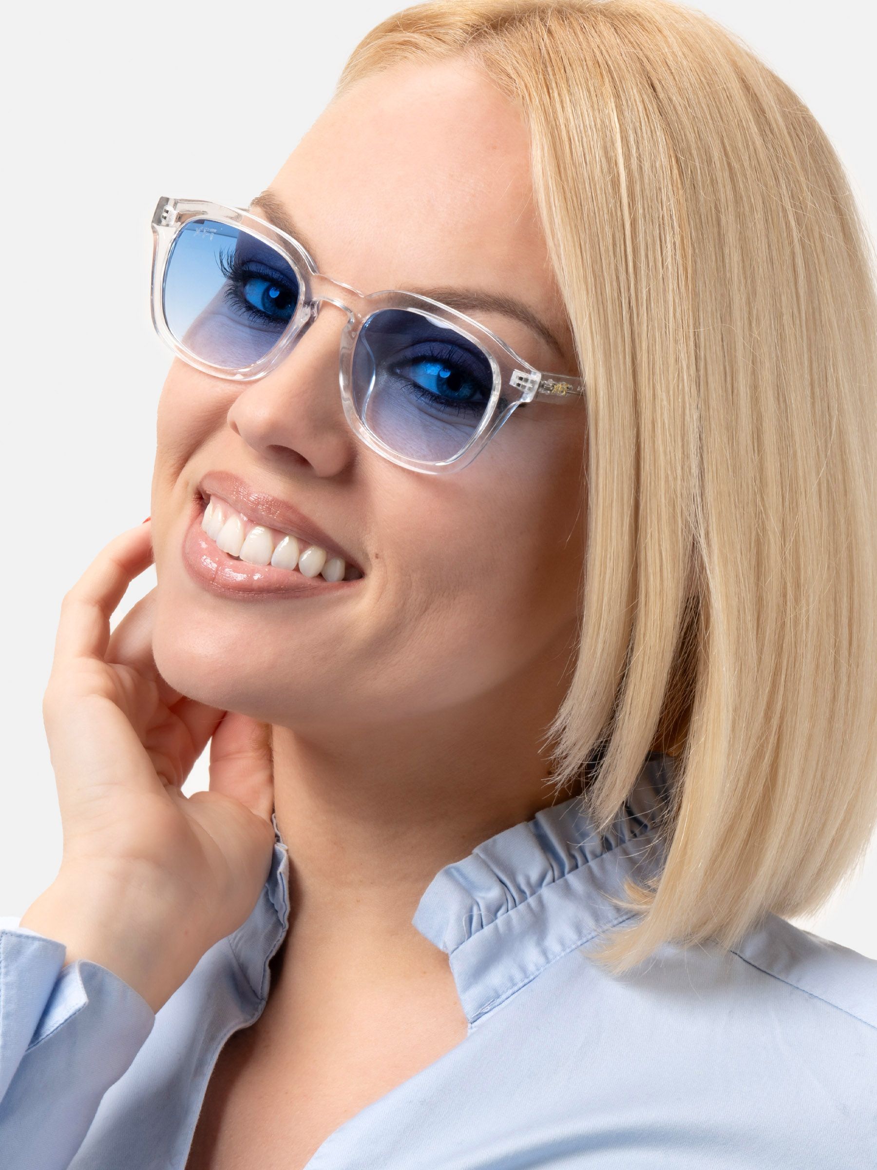 Donna bionda con occhiali da sole trasparenti e lenti blu. Sorride. Camicetta chiara.