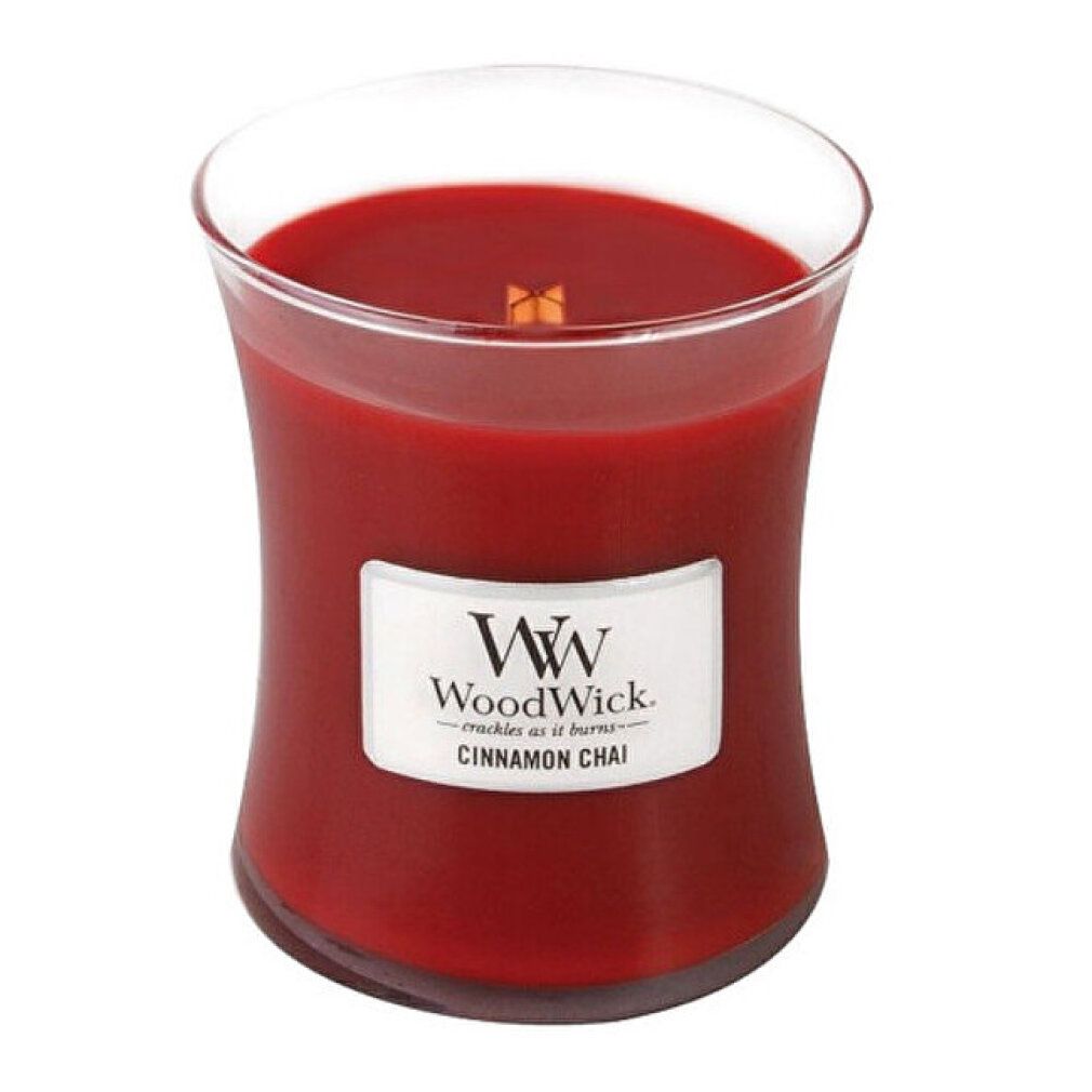 Candela a forma di clessidra con cera rossa. Etichetta bianca con logo e testo: Cinnamon Chai. Stoppino in legno visibile.