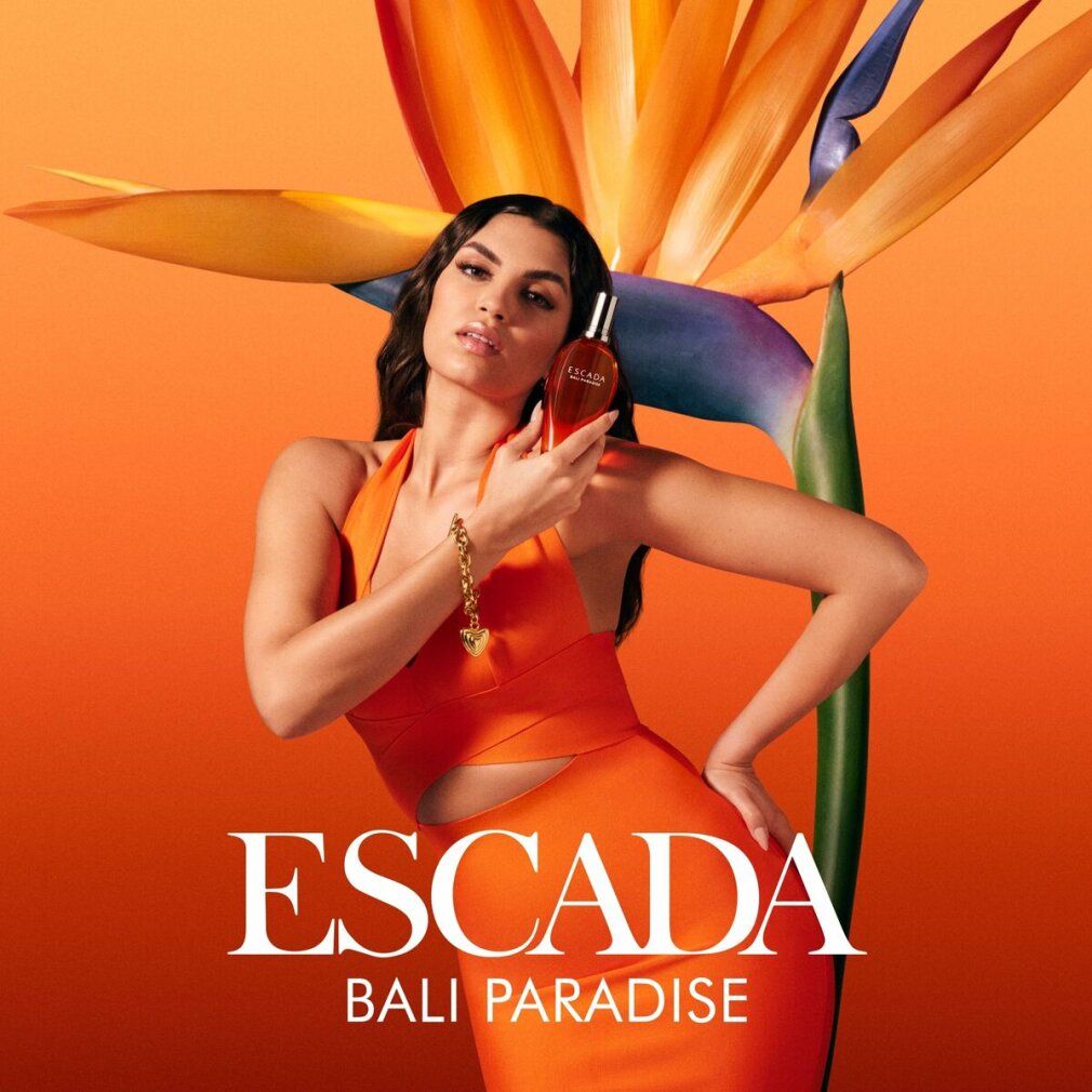 Donna tiene un flacone. Scritta: ESCADA BALI PARADISE. Sfondo arancione.